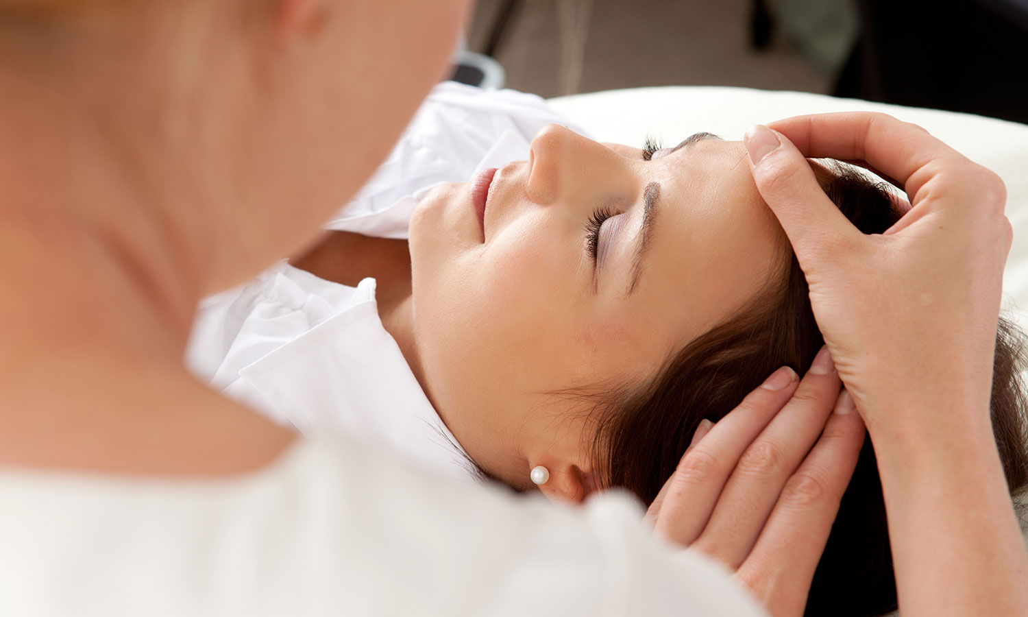 Naheaufnahme einer liegenden Frau mit geschlossenen Augen, die von der Therapeutin eine Stirnmassage erhält. -yler Olson/Shutterstock.com