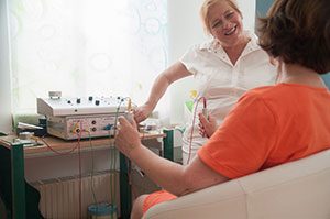 Bioresonanz – Behandlung Patientin, mit Rücken zum Betrachter und speziellen Bioresonanz-Metallstiften in den Händen im Gespräch mit der behandelnden Ganzheitsmedizinerin. - Jamina Paukner/Pumperlgsund