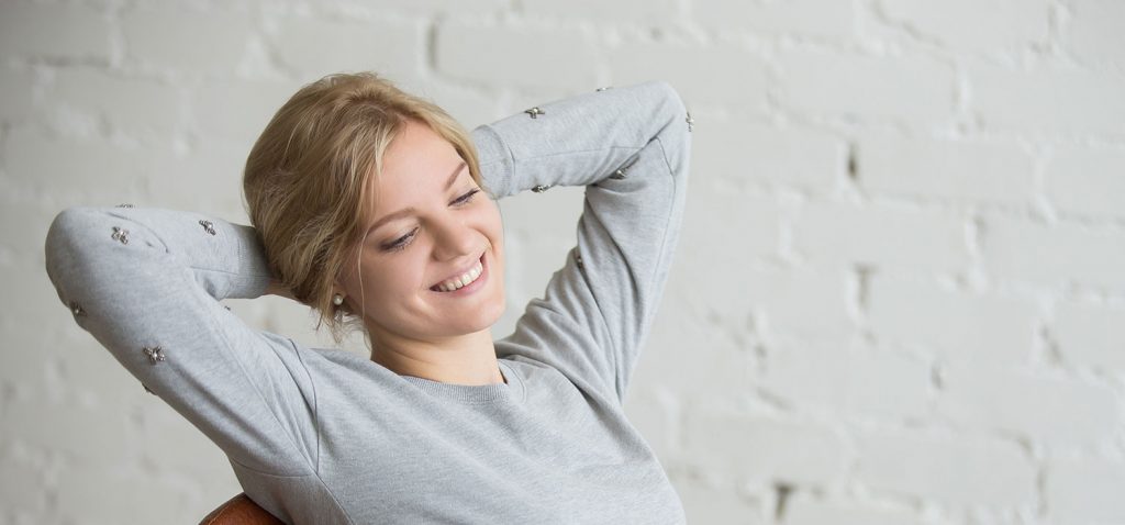 Frau in grauem Sweater, die Arme hinter dem Kopf haltend. - fizkes/Shutterstock.com
