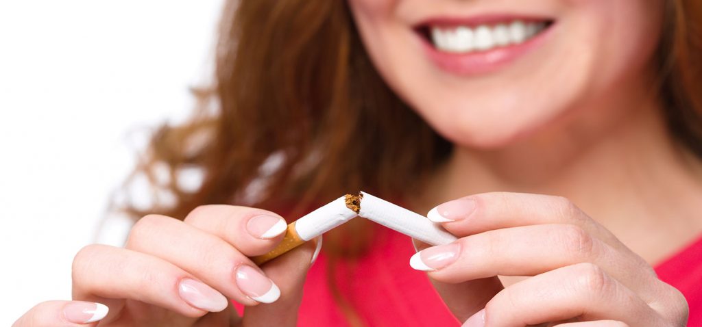 Frau in Nahaufnahme mit zufriedenem Lächeln. Vor sich in den Händen eine Zigarette, die sie soeben zerbricht. -Serhiy Kobyakov/Shutterstock.com
